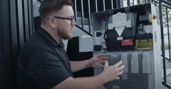 A man examines electronic components inside an open network enclosure outdoors.